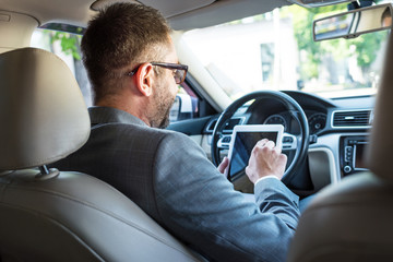 partial view of businessman in eyeglasses using tablet in car