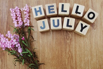 hello july with artificial flower on wooden background