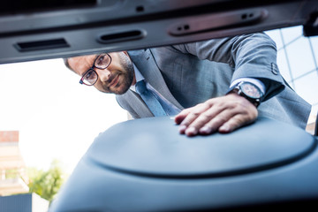 selective focus of businessman in eyeglasses putting luggage into car on parking