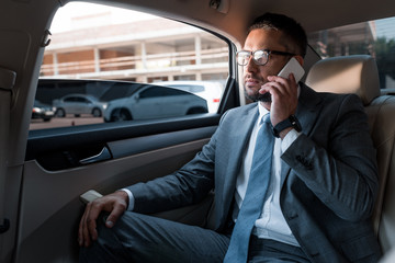 businessman talking on smartphone on backseat in car