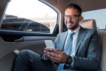 smiling businessman using smartphone on backseat in car