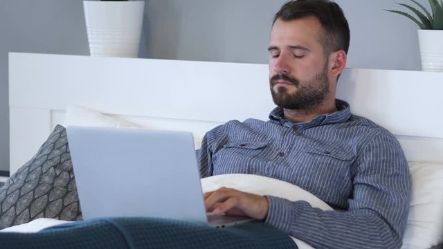 Man Working on Laptop while Relaxing in Bed