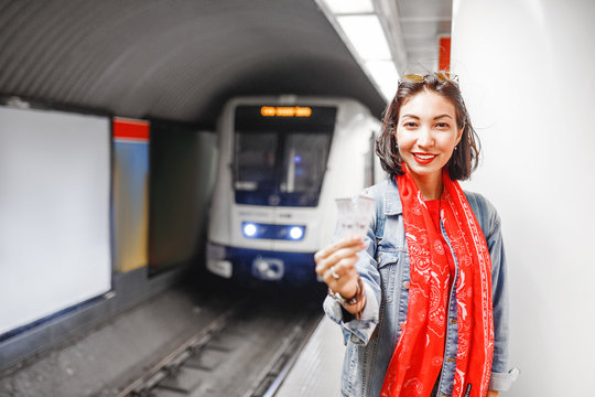 The woman shows two tickets at the background of the approaching train in the subway. Concept of urban public underground transport