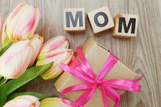 mom with gift box present and flower bouquet on wooden background