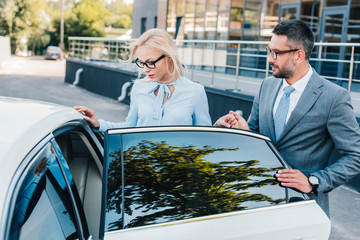 portrait of businessman helping colleague sit into car on street