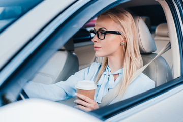 side view of blonde businesswoman with coffee to go driving car