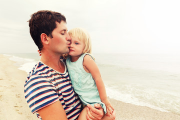 Father holds daughter on his hands and kisses her on the forehead. Family vacation by the sea.