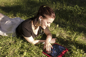 beautiful girl lies on grass and looks at tablet