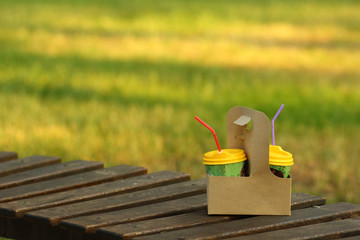 Obraz na płótnie Canvas Cardboard coffee to go carrier, place for logo mockup, in the sunlit summer park on wooden bench