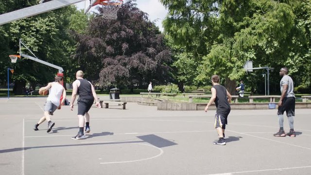 Young men playing basketball on an outdoor court in summer 