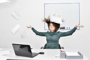 The brown-haired girl happy in the office behind the laptop threw up papers and documents.