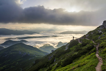 Wide mountain panorama. Small silhouette of tourist with backpack on rocky mountain slope pointing...