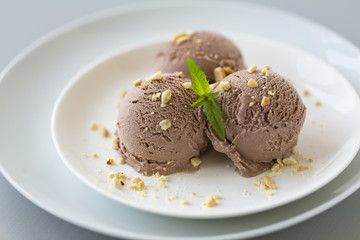 Tasty homemade bowl of chocolate ice cream with mint and nuts on a light background. 