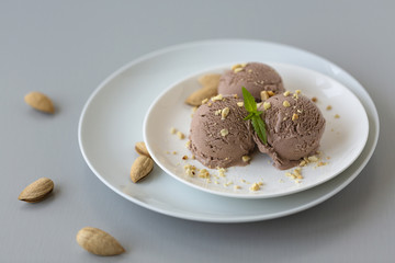 Tasty homemade bowl of chocolate ice cream with mint and nuts on a light background. 