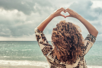 Woman with beautiful curly hair making heart gesture at the sea