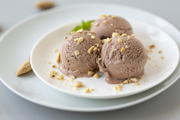 Tasty homemade bowl of chocolate ice cream with mint and nuts on a light background. 