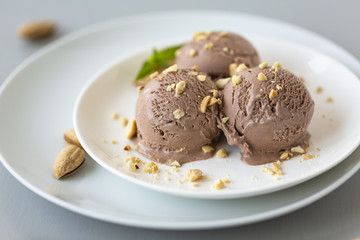 Tasty homemade bowl of chocolate ice cream with mint and nuts on a light background. 