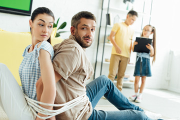 parents sitting tied with rope on floor and children holding clipboard at home