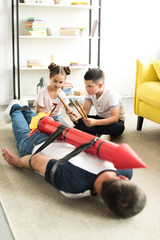 tied dad with rocket toy lying on floor and children playing with him