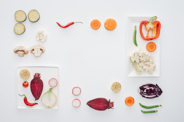 top view of square white plates and fresh sliced vegetables isolated on white