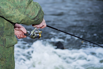 Male angler catches on a spinning reel the fish in fast water in the offseason.