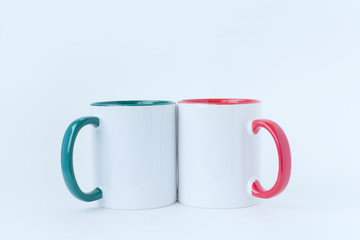 Two white mugs, with a green and red handle on a light background. 