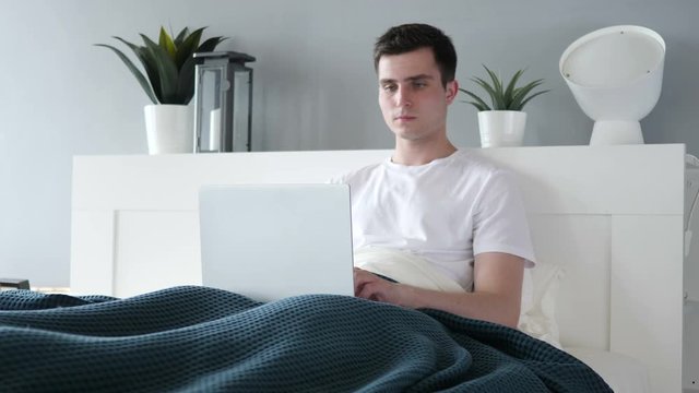 Man Working on Laptop while Relaxing in Bed