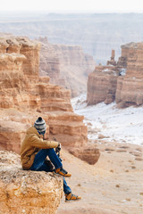 A cheerful traveler with a camera sits on the edge of a cliff in the Charyn canyon in Kazakhstan. Analogue of the American Grand Canyon.