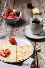 Openwork thin cheese crepes served with strawberry on wooden background. Homemade pancakes. Delicious breakfast