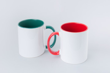 Two white mugs, with a green and red handle on a light background. 