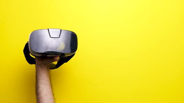 Man hand holding and rising a VR virtual reality headset over an yellow background