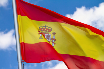 Flag of Spain waving in the wind on flagpole against the sky with clouds on sunny day, close-up