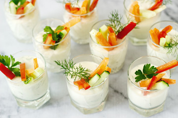 Snack in a glass with fresh cream and various vegetables on a light background.