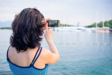 A brunette woman is making a photo of a yacht