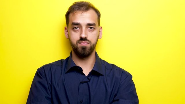 Young beautiful man looks at his right and left them makes the silence gesture by bringing his finger to the mouth. Close up footage over yellow background