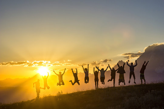 group of people with hands up jumping on grass in sunset mountains