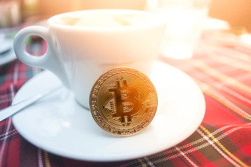 Cup of coffee with bitcoin on it. Sun leaks from the right side.