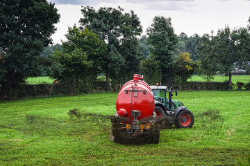 Farmer spraying liquid manure by use of a slurry tanker on a green meadow. 