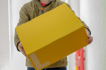 Briefträger mit großem gelbem Paket an Wohnungstür