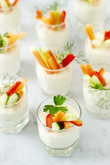 Snack in a glass with fresh cream and various vegetables on a light background.