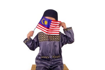 Young Malay Asian boy wearing Malay traditional clothe baju melayu with skull cap or songkok holding and waving Malaysia flag isolated on white