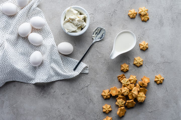 flat lay with cut butter, sour cream, cookies and raw chicken eggs ingredients for making pie on grey surface