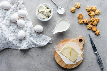 flat lay with cut butter, cookies and raw chicken eggs ingredients for making pie on grey surface