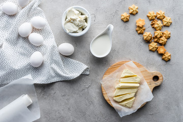 flat lay with cut butter, sour cream, cookies and raw chicken eggs ingredients for making pie on grey surface