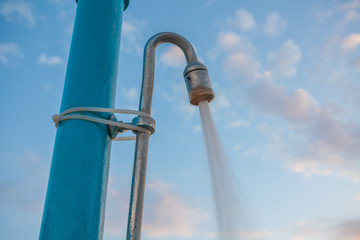 Tall post with pipe mounted. Strong water pressure flowing from the shower head. Cable tying the metal assembly. Beach set up for cleansing the body. Rejuvenate after the sun exposure.