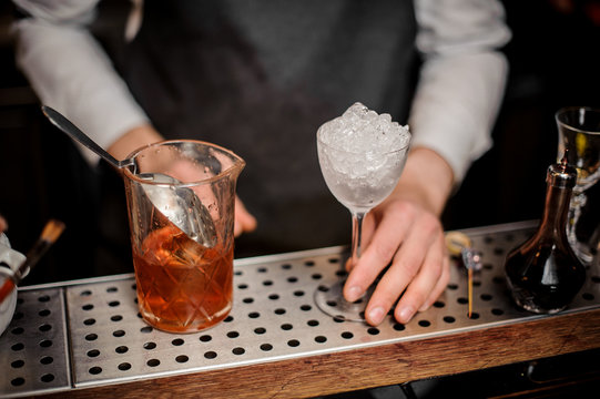 Bartender holding a glass filled with ice and alcoholic drink