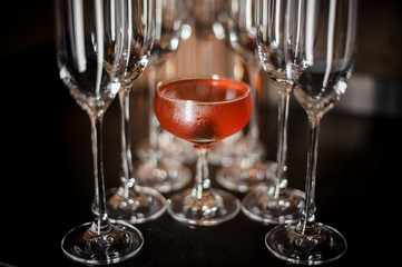 Elegant cocktail glass filled with tasty red alcoholic cocktail among empty champagne glasses