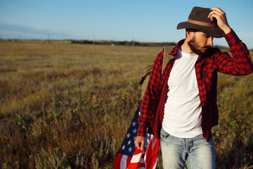 4th of July. American Flag.Patriotic holiday. Traveler with the flag of America. The man is wearing a hat, a backpack, a shirt and jeans. Beautiful sunset light. American style. 