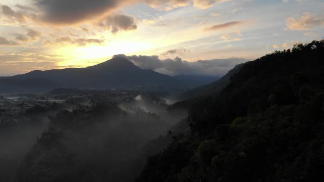 Ungraded aerial clip of beautiful sunrise behind a mountain overlooking a foggy valley in the morning at Tebing Keraton.