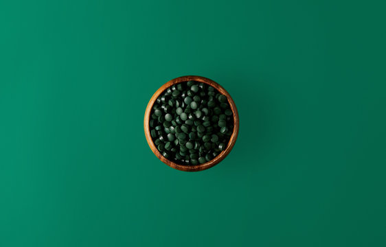 top view of wooden bowl with pile of spirulina pills isolated on green